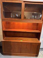 Full view of the mid-century entertainment unit showing the upper shelving with sliding glass doors and open middle shelves above the lower storage cabinet.