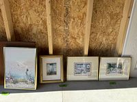 Wide view of four framed prints against a wooden wall, showing an overview of the lot.