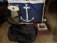 Photo shows all four items: navy dog bed with anchor design, maroon couch cover in packaging, beige/navy tote with paw print, and black duffel tote all placed on floor.