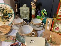 Front view of three ceramic cups with matching saucers, decorative plates, and Asian-inspired figurines on display.
