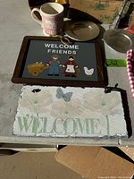 Wooden frame with a 'WELCOME FRIENDS' sign, ceramic mug, metal plate, and various decorative items.