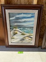 Framed canvas painting of a seaside dune with beach grass and ocean waves under cloudy sky, signed by artist.