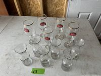 Full set of 13 glasses including five Stella Artois chalice beer glasses and eight smaller assorted clear glasses.