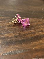 Close-up of pink square-cut stones set in 14k solid gold posts and butterfly backs, showing one earring lying flat and the other upright.
