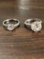 Two rings with clear stones on a wooden surface showing size and details of bands and stones