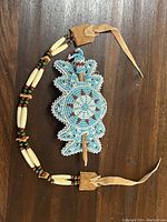 Photo of two Indigenous beaded pieces including a blue and white floral patterned hairpiece and a bone and beaded necklace.