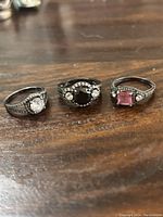 Front view of three blackened sterling silver rings showing clear, black, and pink center stones with clear accent stones