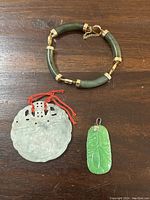 Top view of jade bracelet, translucent carved jade pendant, and bright green leaf-shaped jade pendant on wood surface.