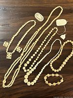 Photo showing large lot of carved Asian-style jewelry including necklaces, bracelets, and carved pendants laid on a wood surface.