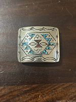 Front of the Navajo belt buckle showing inlaid turquoise and red stones with hallmark and engraved designs.