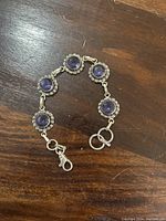 Full view of the silver bracelet with five purple amethyst circular stones set in silver decorative bezels connected by silver links, clasp shown.