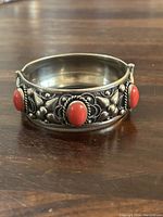 Front view of a silver bangle featuring three oval coral stones and detailed silver work.