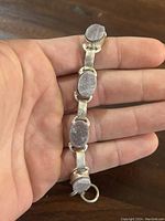 Handheld image showing silver bracelet with five oval stone settings and toggle clasp, illustrating size and detail of stones and metalwork.