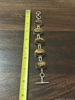 Silver Tiger's Eye bracelet laid next to a measuring tape showing length approximately 7.5 inches.