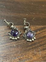 Front view of sterling silver amethyst earrings showing round amethyst cabochons, decorative silver setting and screw back closures.