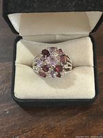 Ring in black velvet box, showing top view of multi-colored gemstones set in sterling silver band.