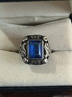 Front view of the sterling silver ring showing the rectangular blue glass stone and floral ornate design around bezel and shoulders.