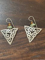 Pair of sterling silver Celtic knot design earrings with amber and green beads on a wooden surface.