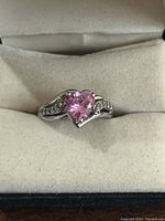 Close-up photo of sterling silver ring with pink heart-shaped centerpiece stone sitting in a cushioned ring box.