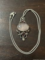 Sterling silver chain necklace with an oval rose quartz pendant and two smaller dark stones, laid on a wooden surface.