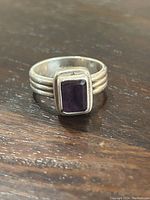 Close-up of sterling silver ring with rectangular amethyst stone on wooden surface