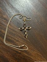 Cross pendant laid flat with chain on wooden surface, showing full necklace and pendant design