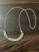 Full view of sterling silver chain and curved jade pendant necklace laid flat on dark wooden surface.