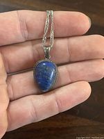 Close-up of the teardrop-shaped lapis lazuli pendant held in hand, showing gold flecks and polished silver bezel setting.