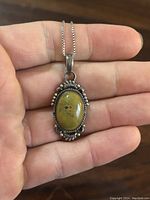 Close-up of oval yellow stone pendant set in ornate sterling silver.
