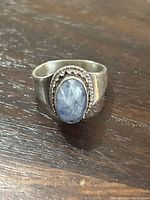 Angle showing blue stone and twisted silver bezel, ring on wood surface.