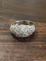 View of the ring placed on wood surface showing the crisscross pattern with small stones and filigree texture