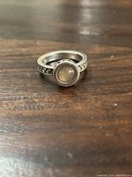 Single sterling silver ring with round smooth cabochon stone on patterned band placed on wooden surface.