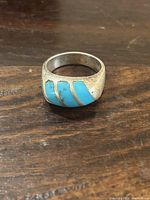 Close-up front view of the sterling silver ring with three diagonal turquoise inlays on a wooden surface.
