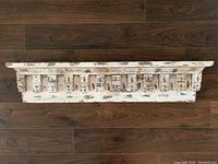 Photo of antique architectural salvage floating shelf showcasing distressed white paint and intricate wooden detailing.