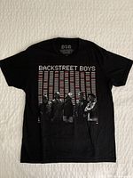 Full front view of the black Backstreet Boys concert T-shirt laid flat on a white textured surface.