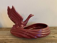 Front and side view of the ceramic swan planter showing its glossy red-purple finish, extended wings, and curved tail reservoir.