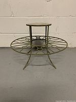 Front view of the metal garden display stand showing circular openwork lower tier, smaller top tier, and three legs.
