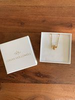 Bee pendant necklace in Logan Hollowell white branded box on wooden surface.