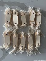 Multiple bundles of rectangular manila tags with attached cotton strings laid out on a flat surface