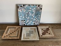 Four square mosaic tile plates with different geometric patterns and pastel color schemes on a wooden surface.