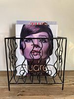 Front view of the black metal magazine holder with books inside showing decorative wire design.