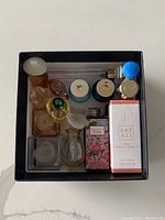 Top-down photo of the open black Prada box containing 16 assorted miniature perfume bottles of various shapes and colors, some boxed.