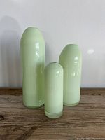 Three pistachio glass vases of varying height arranged side by side on wooden surface against white wall.