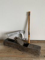 Photo showing all three items: wooden moulding plane, metal bread slicer, and wooden shoe shine tool against a white background