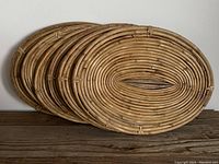 Set of six oval-shaped rattan placemats stacked together showing woven design and size.