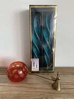 Photo showing all items together: boxed blue twisted taper candles, red etched glass tealight holder, and small brass angel snuffer.