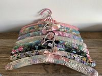 Top view showing nine vintage padded lingerie hangers with floral and pastel fabric covers and bows on hooks.