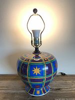 Front image of the vintage Tyndale lamp lit, showing the ceramic base with bright boho celestial patterns, rounded shape, white socket, and brass-colored hardware.