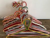 Front angled view of the lot stacking 15 woven fabric vintage hangers with braided hooks and multicolor patterns