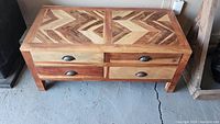 Full view of wooden coffee table showing front and top, four drawers with metal half-moon pulls, and detailed inlaid wood pattern on top.